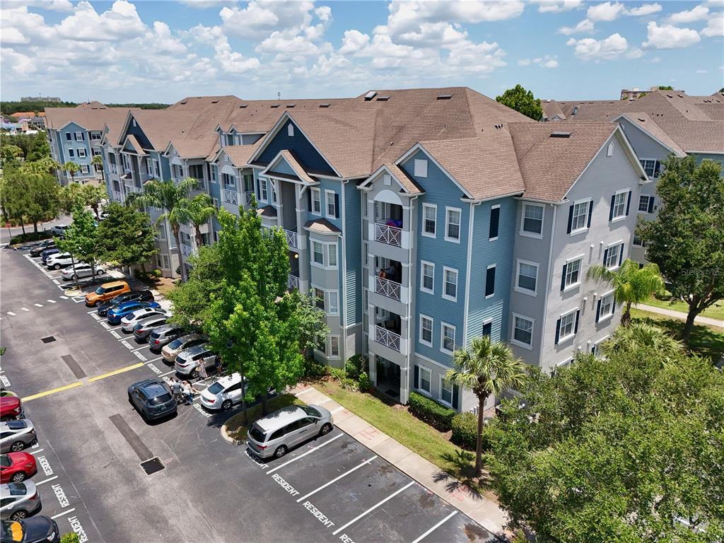 An aerial view shows a multi-story apartment building with blue siding and a parking lot — 5255 CANE ISLAND LOOP UNIT 204, KISSIMMEE, FL