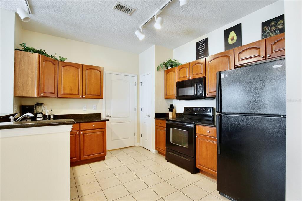 A kitchen features wood cabinets, black appliances, dark countertops, and light-colored tile flooring — 5255 CANE ISLAND LOOP UNIT 204, KISSIMMEE, FL