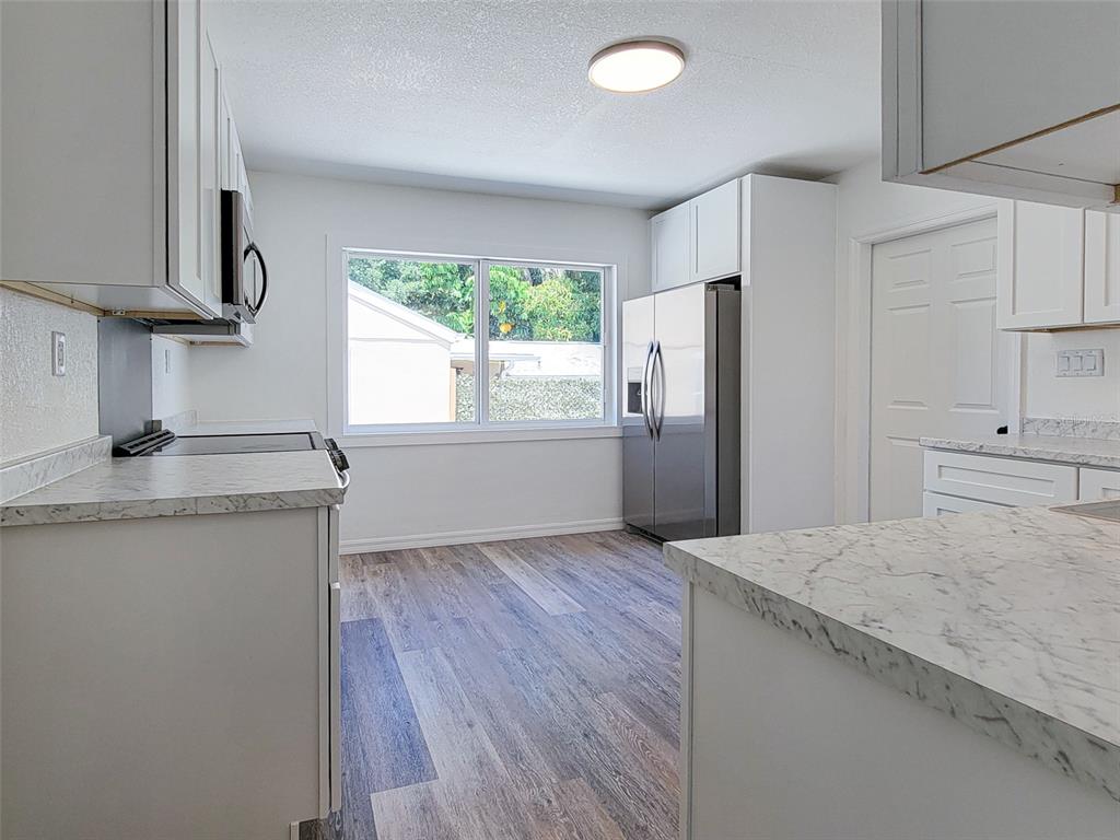 A kitchen features white cabinets, marble-look countertops, stainless steel appliances, and wood-look flooring — 1520 19TH AVENUE W, BRADENTON, FL