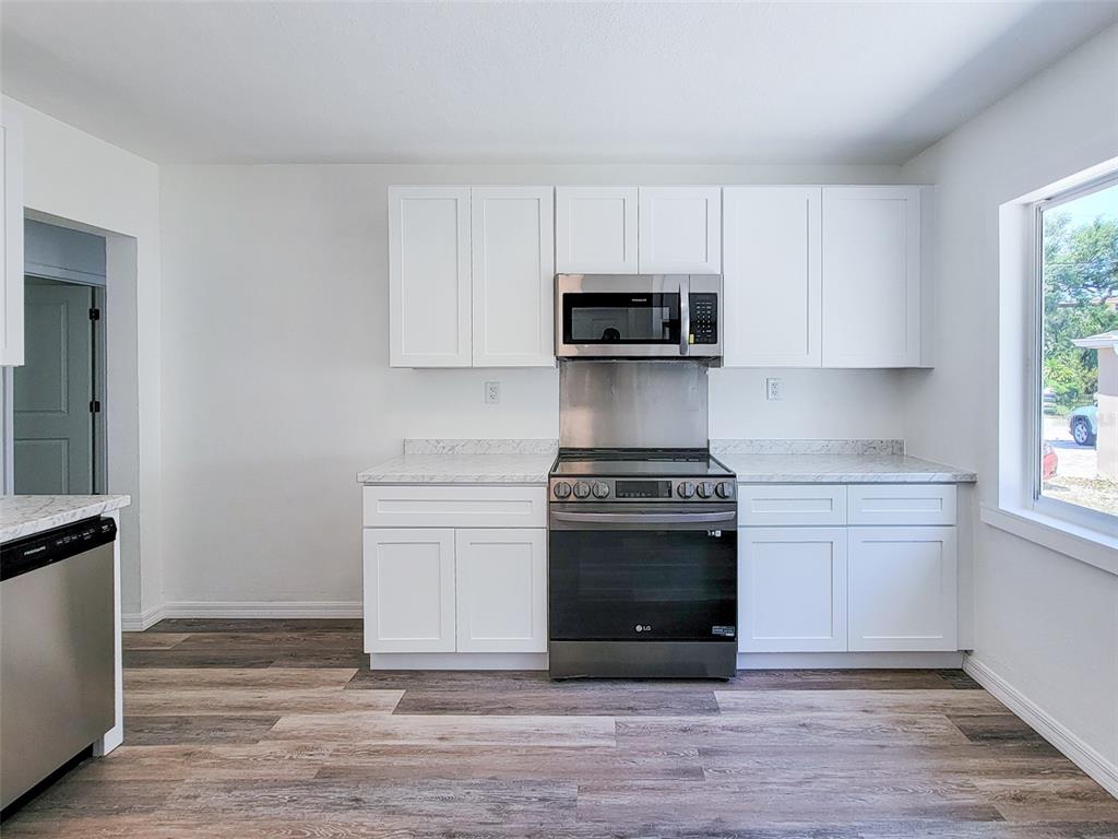 A kitchen features white cabinets, stainless steel appliances, and wood-look flooring — 1520 19TH AVENUE W, BRADENTON, FL