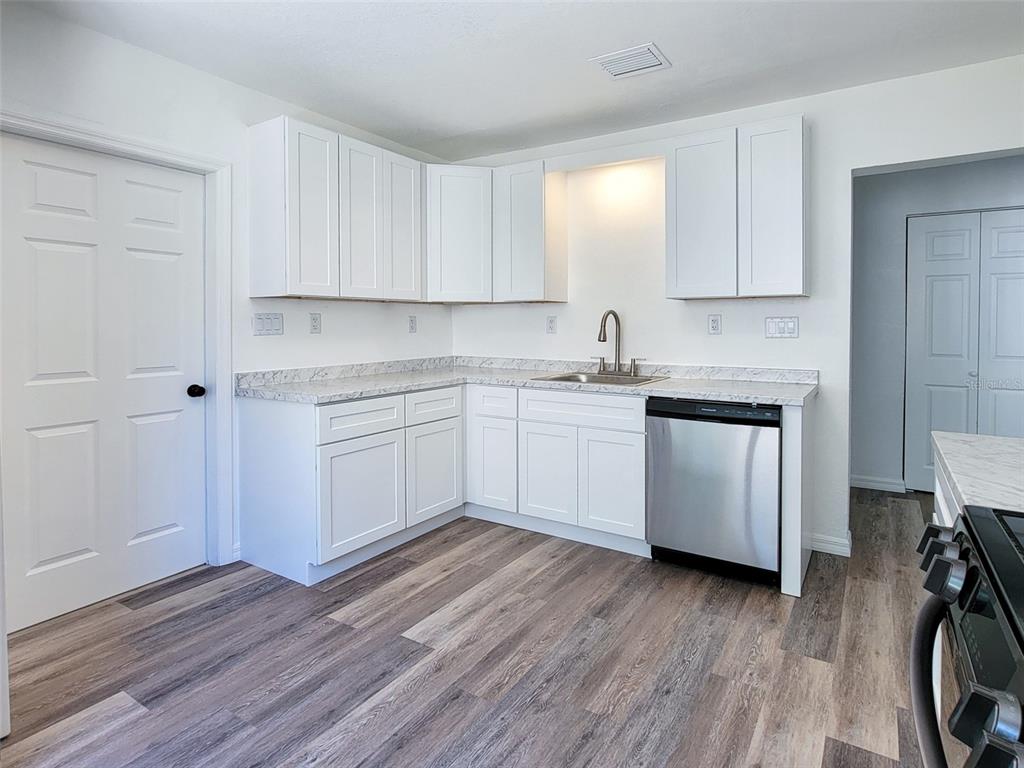 A kitchen features white cabinets, light countertops, a stainless steel dishwasher, and wood-look flooring — 1520 19TH AVENUE W, BRADENTON, FL