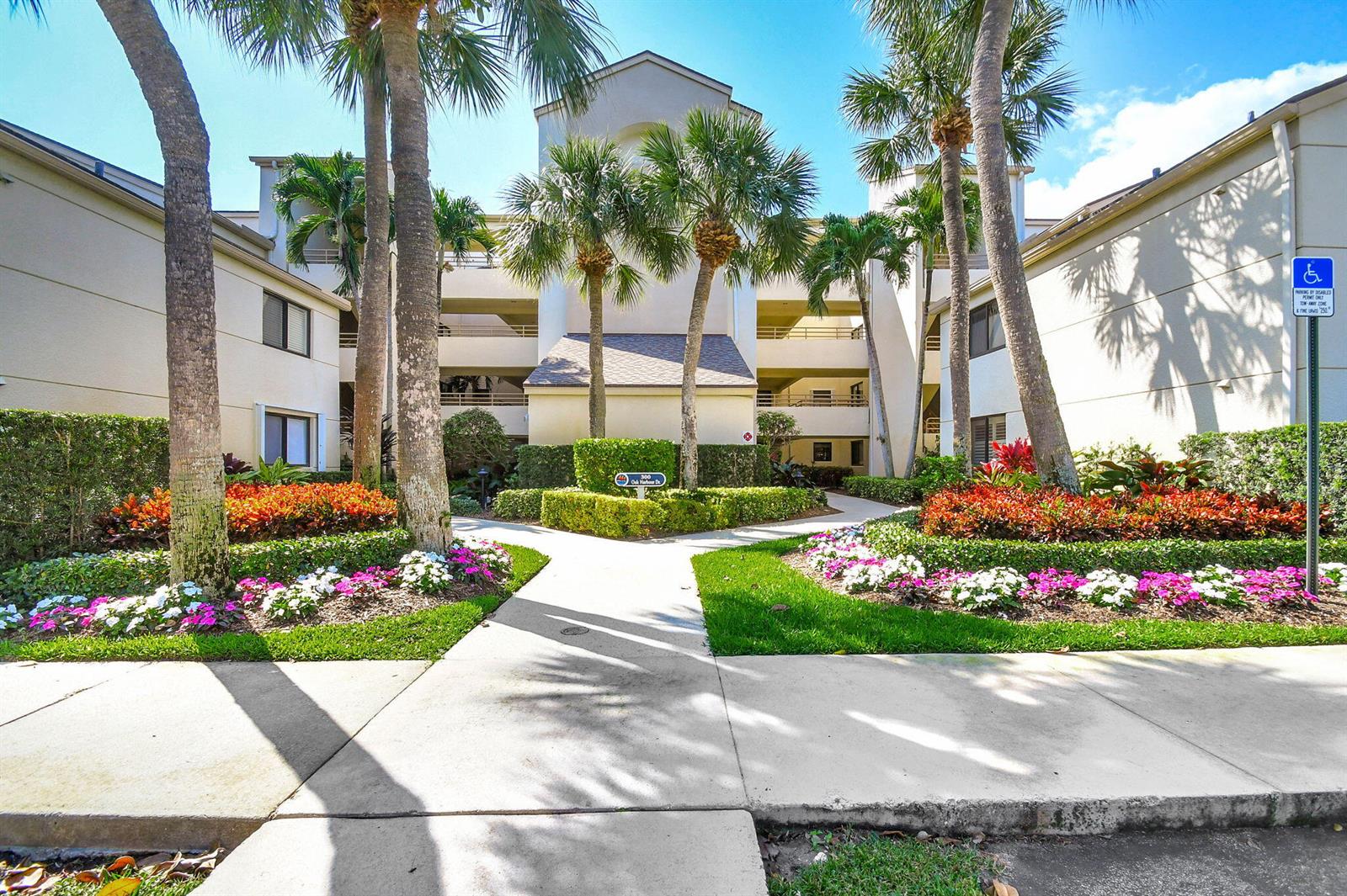 A multi-story apartment building with palm trees and landscaped gardens along a concrete walkway — 318 Oak Harbour Drive # 318, Juno Beach FL 33408, JUNO BEACH, FL