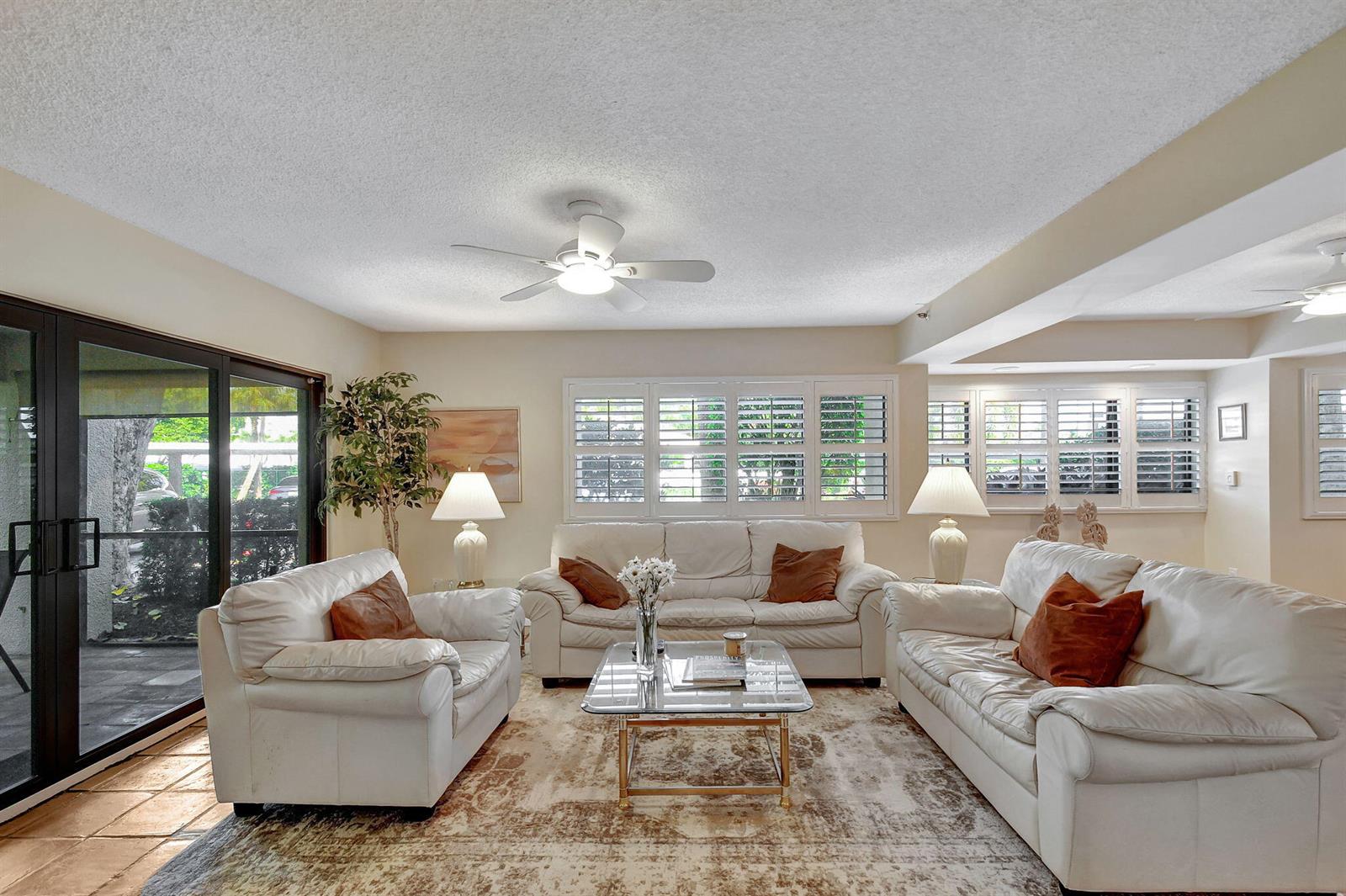 A living room features three white leather sofas, a glass coffee table, and plantation shutters — 318 Oak Harbour Drive # 318, Juno Beach FL 33408, JUNO BEACH, FL