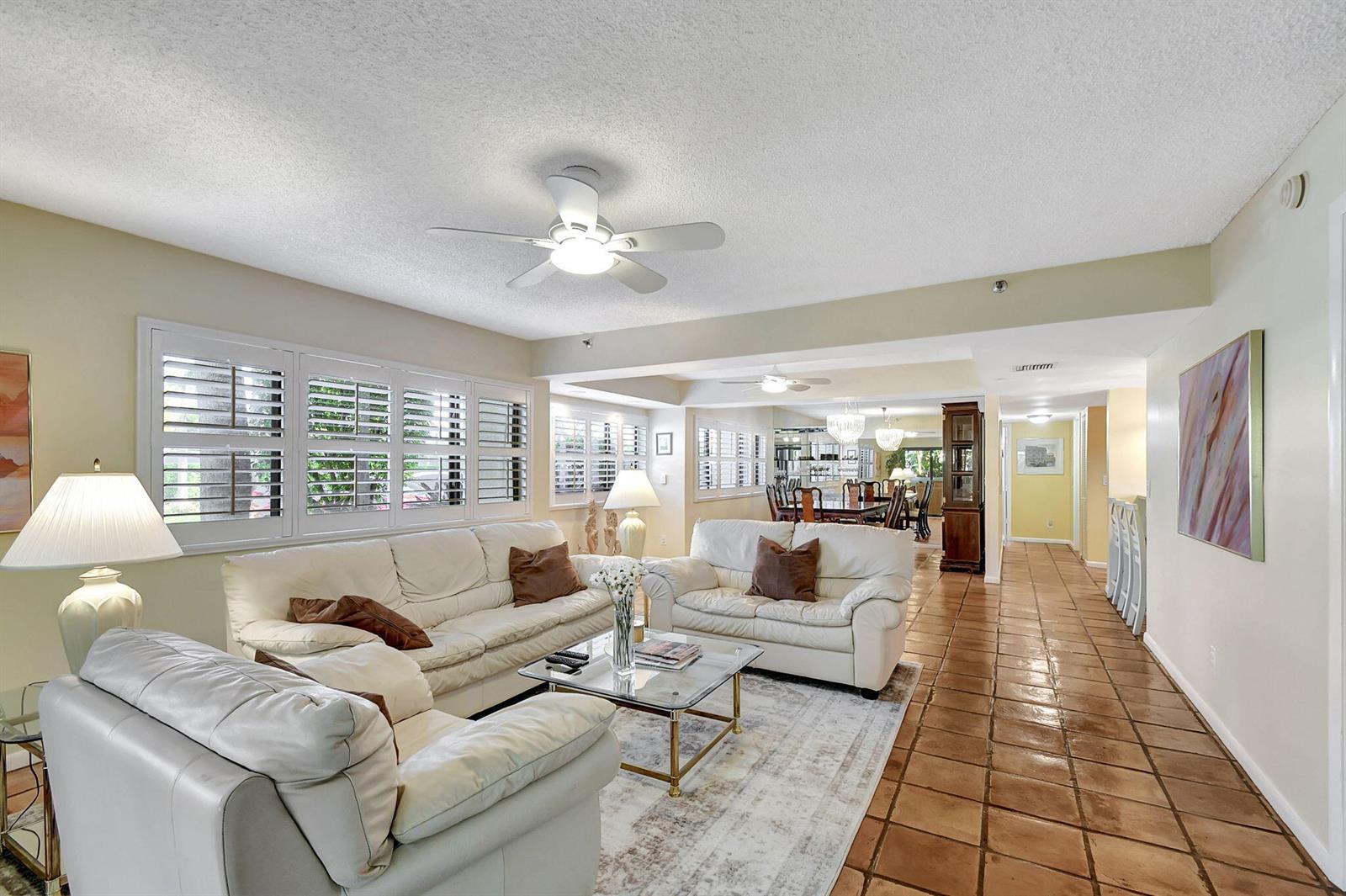 A living room features white leather sofas, a glass coffee table, and terracotta tile flooring — 318 Oak Harbour Drive # 318, Juno Beach FL 33408, JUNO BEACH, FL