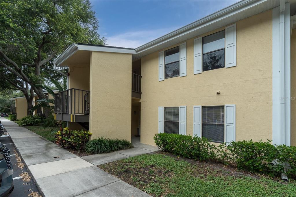 A two-story yellow apartment building with a sidewalk and parking area in the foreground — 3001 58TH AVENUE S UNIT 1211, ST PETERSBURG, FL
