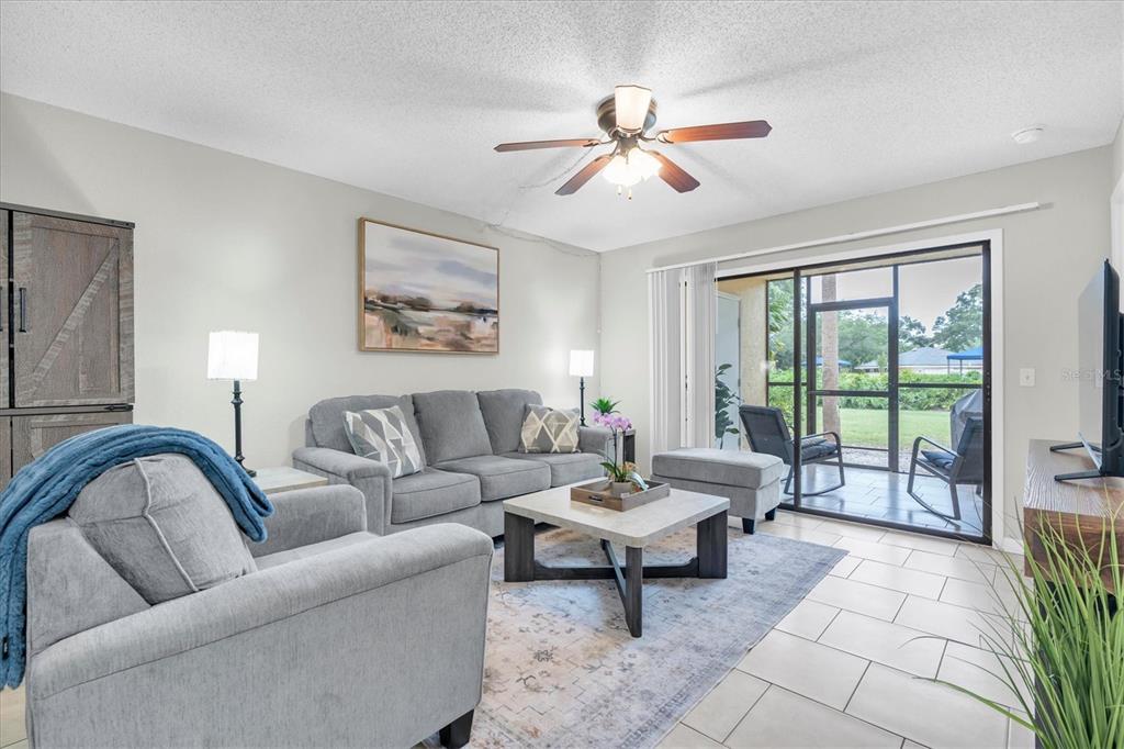 A living room features a gray sofa, armchair, coffee table, and sliding glass doors to a patio — 3001 58TH AVENUE S UNIT 1211, ST PETERSBURG, FL