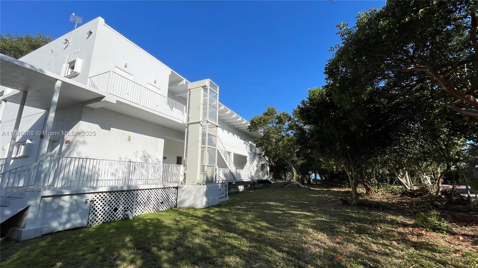 A white multi-story building features an exterior glass elevator shaft and a grassy yard — 14 125th Street Gulf, Marathon FL 33050, MARATHON, FL