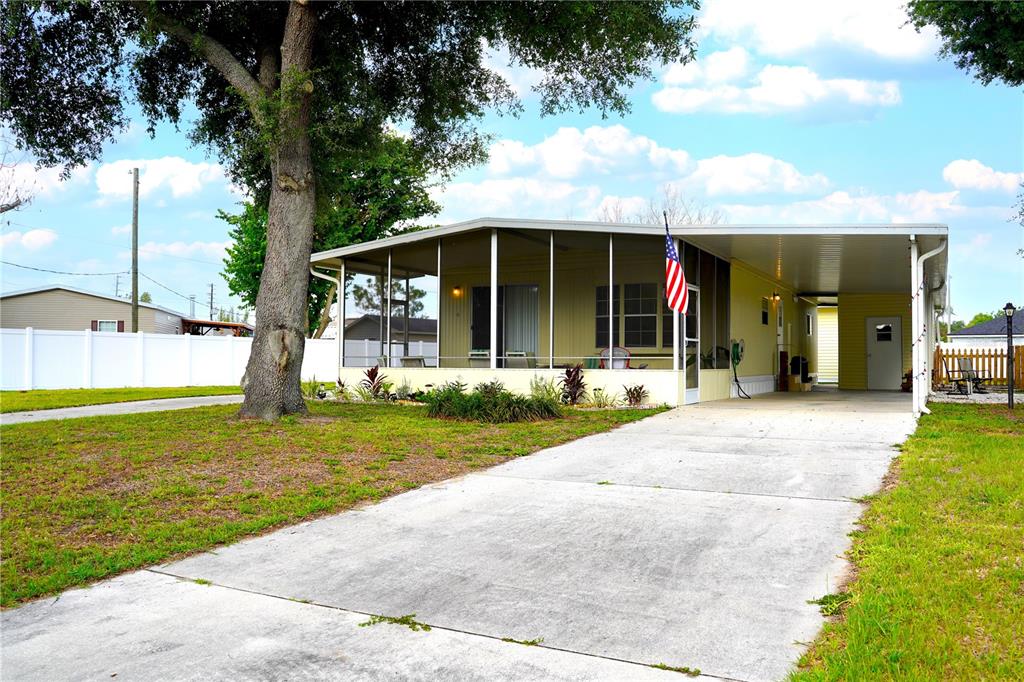 A single-story manufactured home features a screened-in porch, a concrete driveway, and a carport — 5747 E LAKE FOX DRIVE, WINTER HAVEN, FL