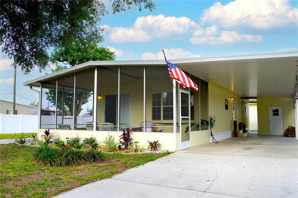 A light yellow manufactured home features a screened-in front porch and an attached carport — 5747 E LAKE FOX DRIVE, WINTER HAVEN, FL