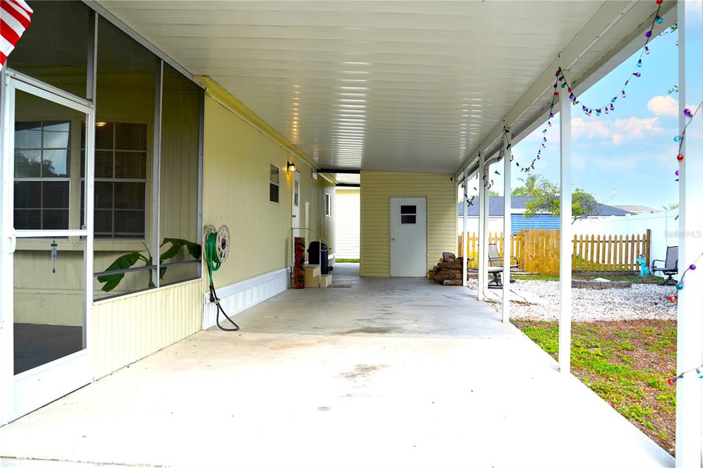 A covered concrete carport extends alongside a mobile home with a screened-in porch — 5747 E LAKE FOX DRIVE, WINTER HAVEN, FL