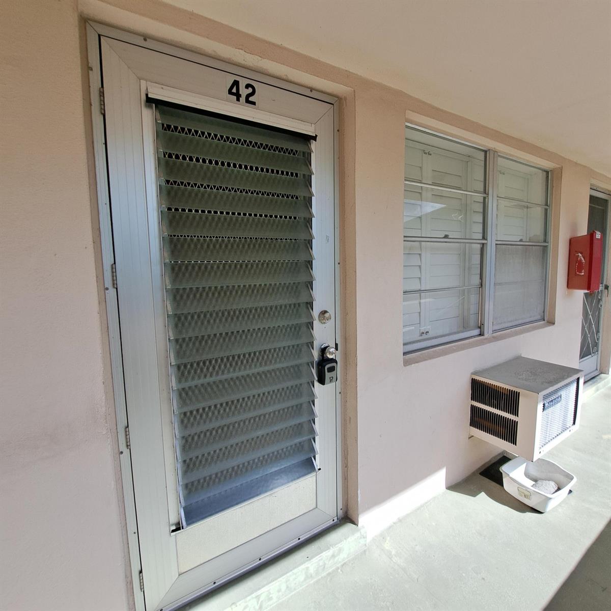 An exterior view of a door numbered 42 with jalousie glass panels and a window unit — 42 Norwich B, West Palm Beach FL 33417, WEST PALM BEACH, FL