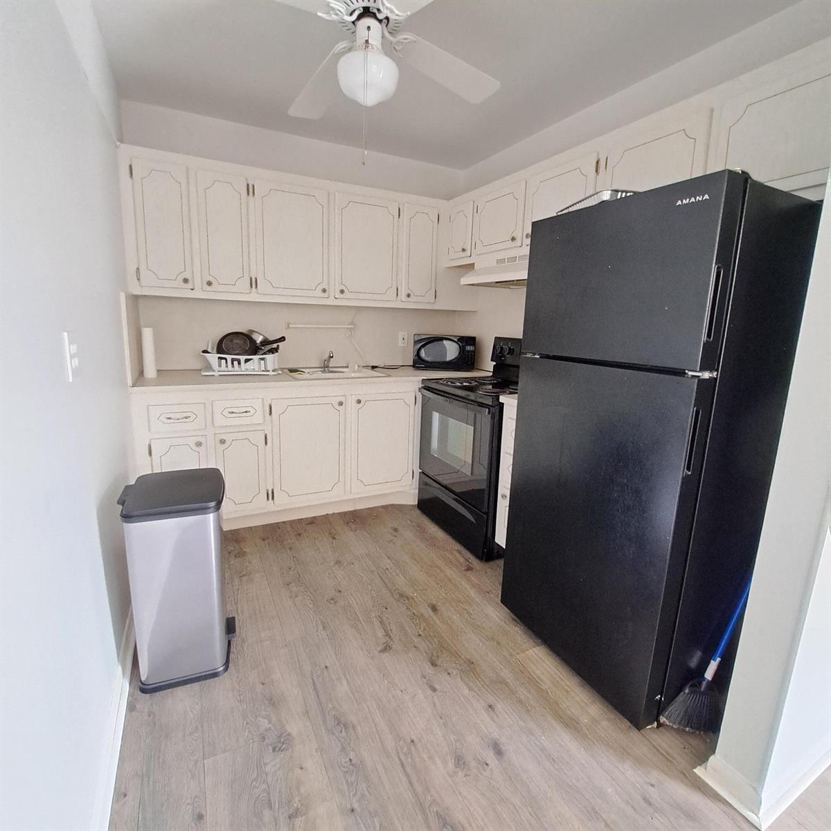 A small kitchen features white cabinets, black appliances, and wood-look flooring — 42 Norwich B, West Palm Beach FL 33417, WEST PALM BEACH, FL
