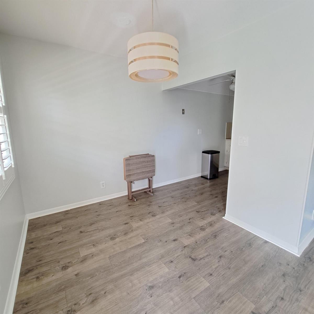 An empty dining area features light gray walls, wood-look flooring, and a modern drum pendant light — 42 Norwich B, West Palm Beach FL 33417, WEST PALM BEACH, FL