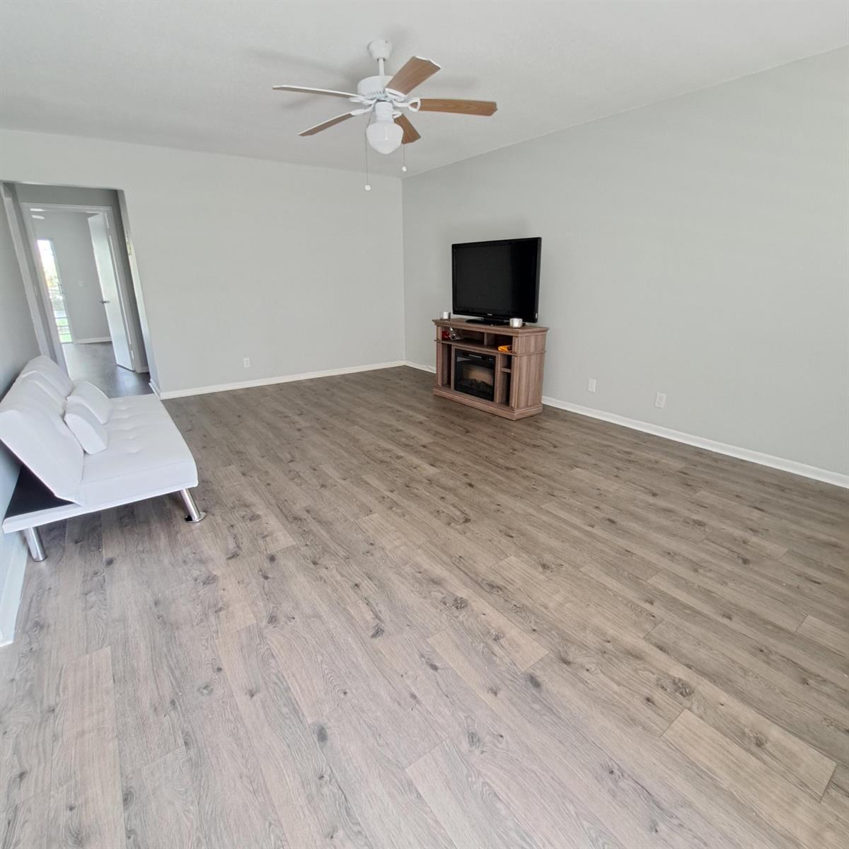 A living room features light gray walls, wood-look flooring, a white futon, and a television console — 42 Norwich B, West Palm Beach FL 33417, WEST PALM BEACH, FL