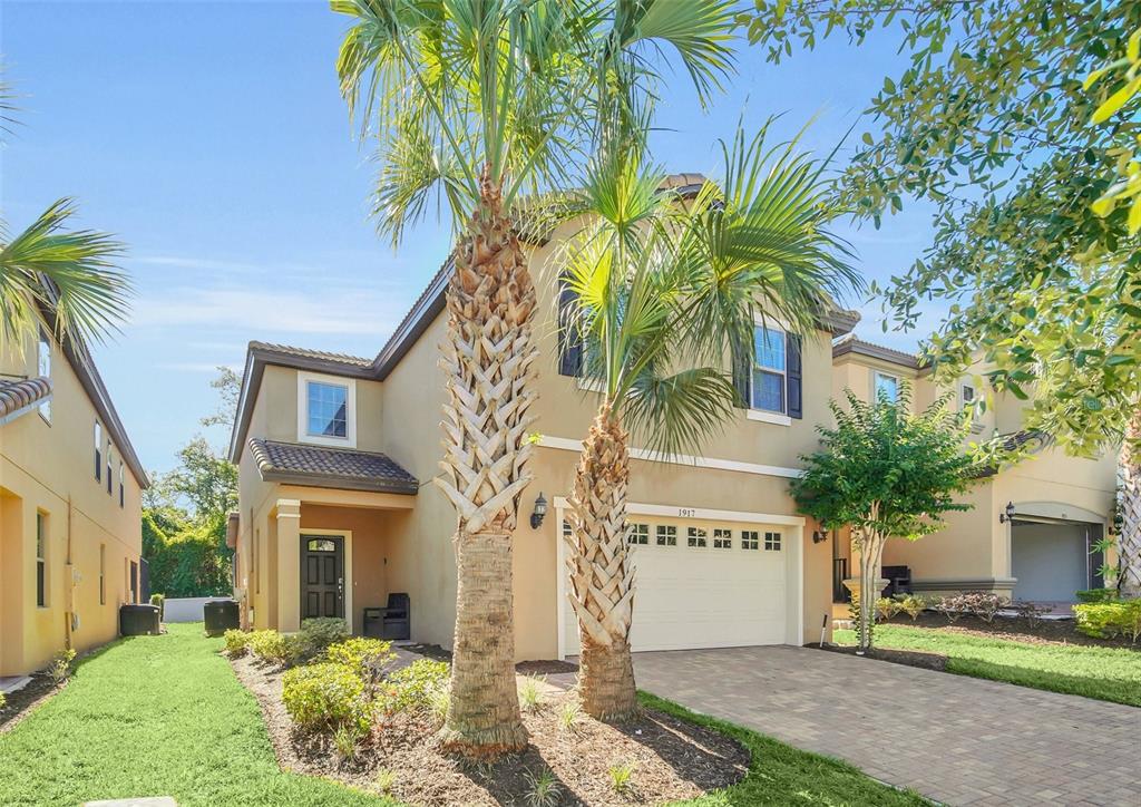 A two-story tan stucco house with a paved driveway and two palm trees in front — 1917 NICE COURT, KISSIMMEE, FL