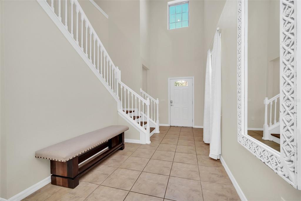 An entryway features a staircase with white railings, tile flooring, a bench, and a mirror — 1917 NICE COURT, KISSIMMEE, FL