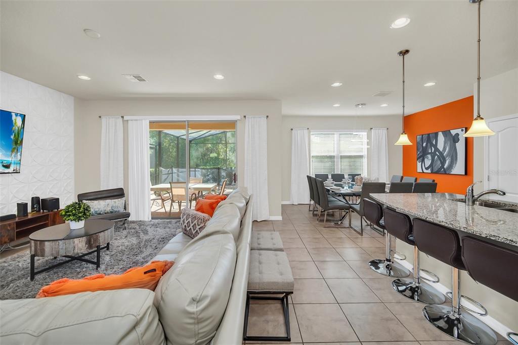 An open-concept living and dining area features tile floors, an orange accent wall, and kitchen seating — 1917 NICE COURT, KISSIMMEE, FL