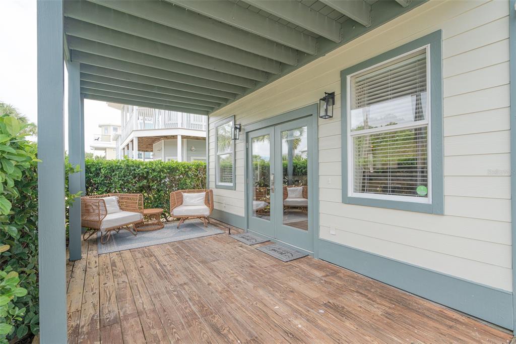 A covered wooden porch features two wicker chairs, a small table, and glass double doors — 79 MARK STREET, DESTIN, FL