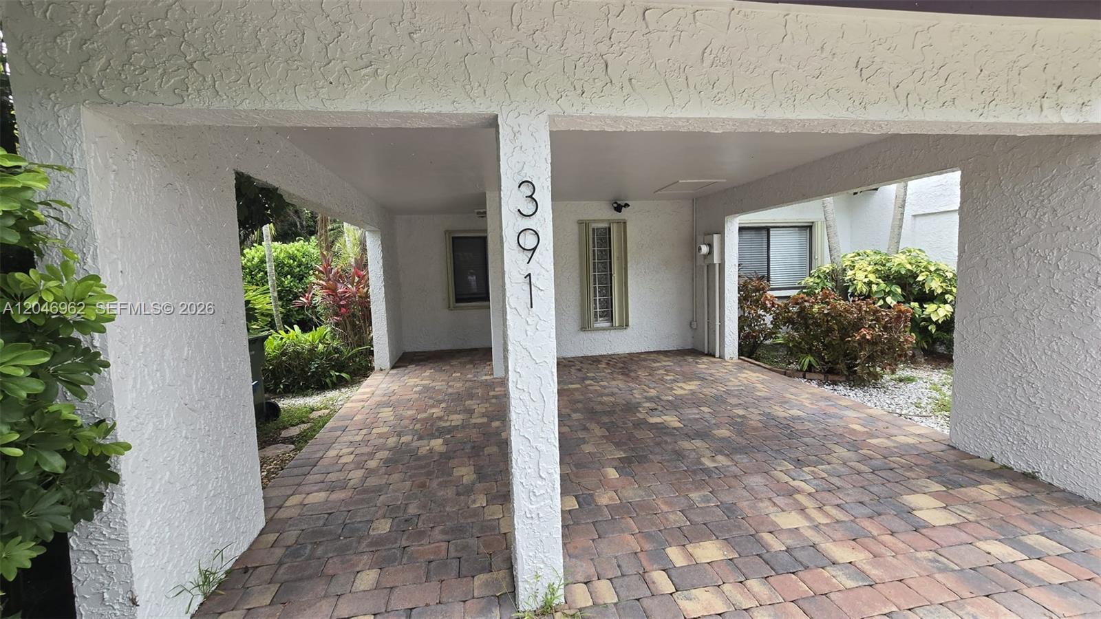 A covered carport features a paver floor and a white stucco support pillar with numbers — 391 Ivy Ln # 1, Weston FL 33326, WESTON, FL