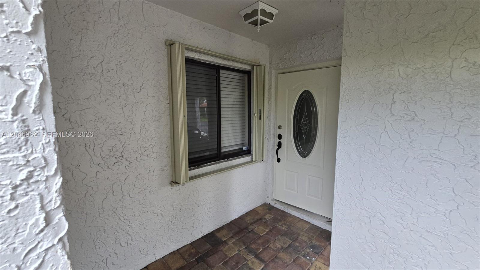 A white front door and a window with shutters are set in a stucco entryway — 391 Ivy Ln # 1, Weston FL 33326, WESTON, FL