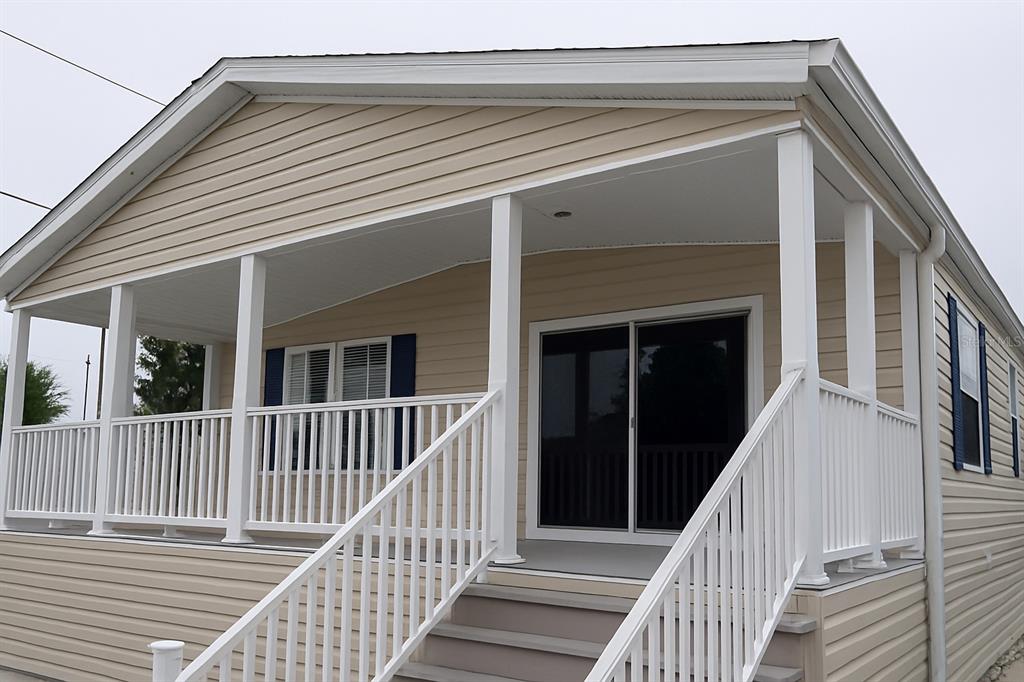A beige mobile home features a covered front porch with white railings and stairs — 1375 PASADENA AVENUE S UNIT 217, SOUTH PASADENA, FL