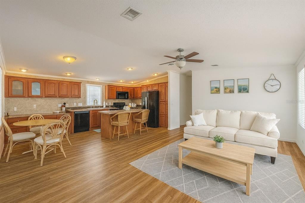 An open-concept living room and kitchen feature wood-look flooring, light-colored furniture, and wooden cabinetry — 1375 PASADENA AVENUE S UNIT 217, SOUTH PASADENA, FL
