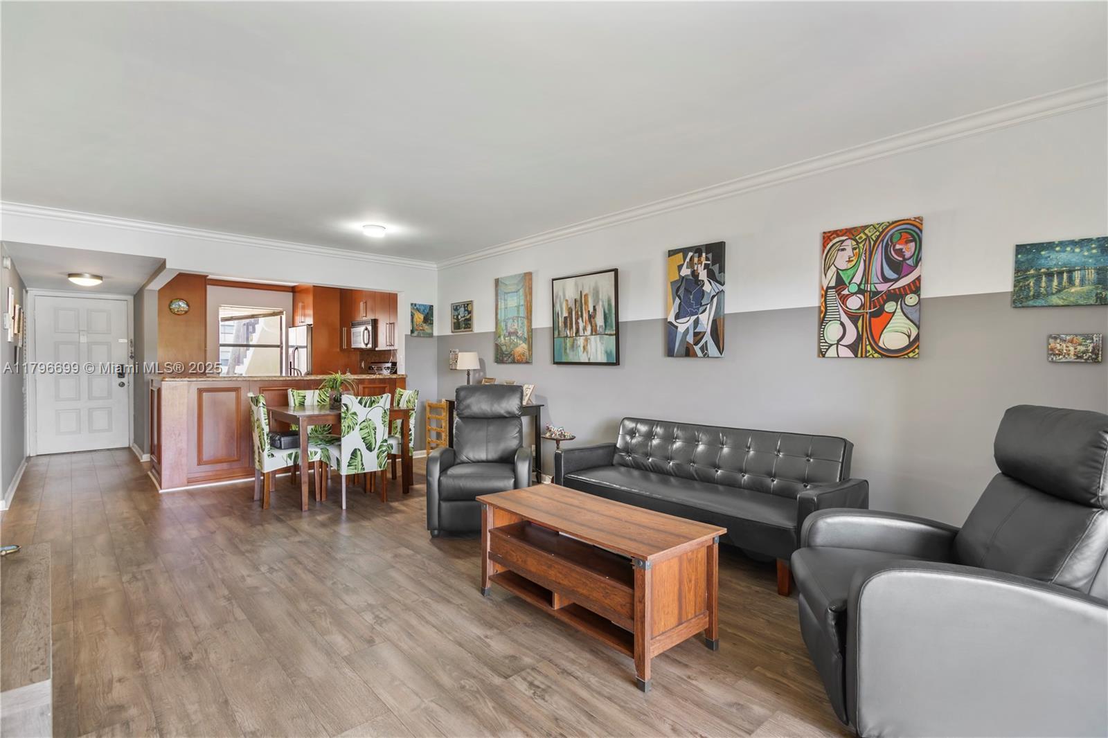 A living room with wood flooring, a black sofa, two recliners, and an adjacent dining area — 22053 Palms Way # 106, Boca Raton FL 33433, BOCA RATON, FL