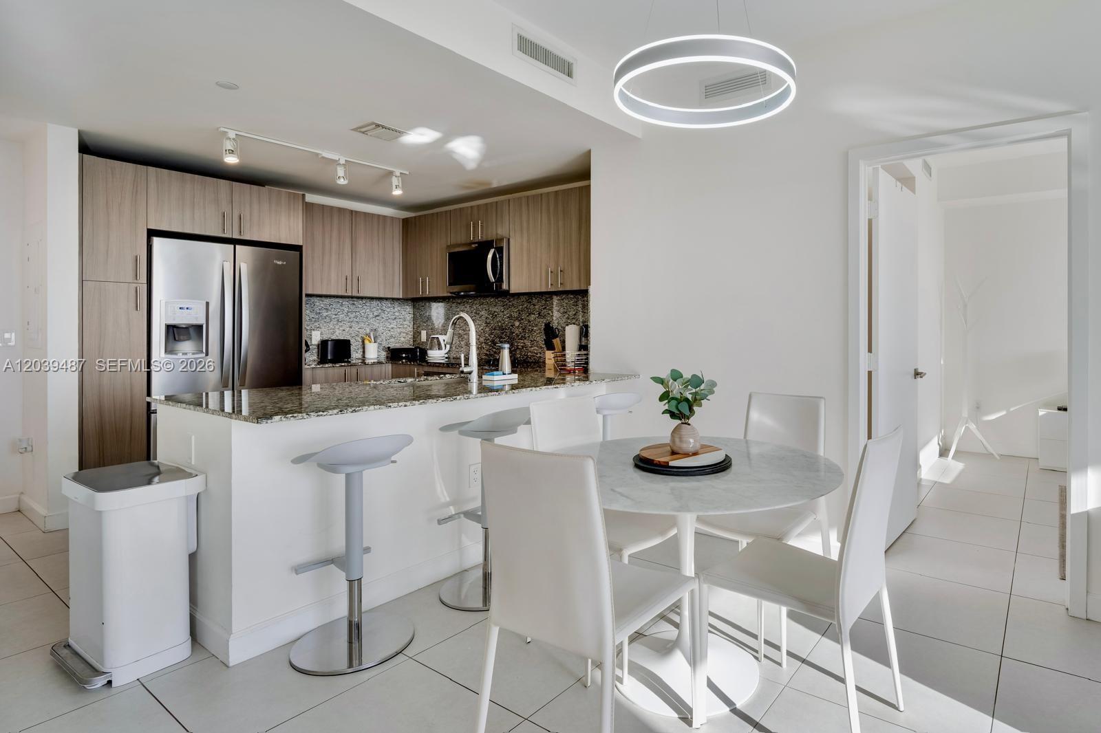 A modern kitchen with wood cabinets and granite countertops opens to a small dining area — 5350 NW 84th Ave # 909, Doral FL 33166, DORAL, FL