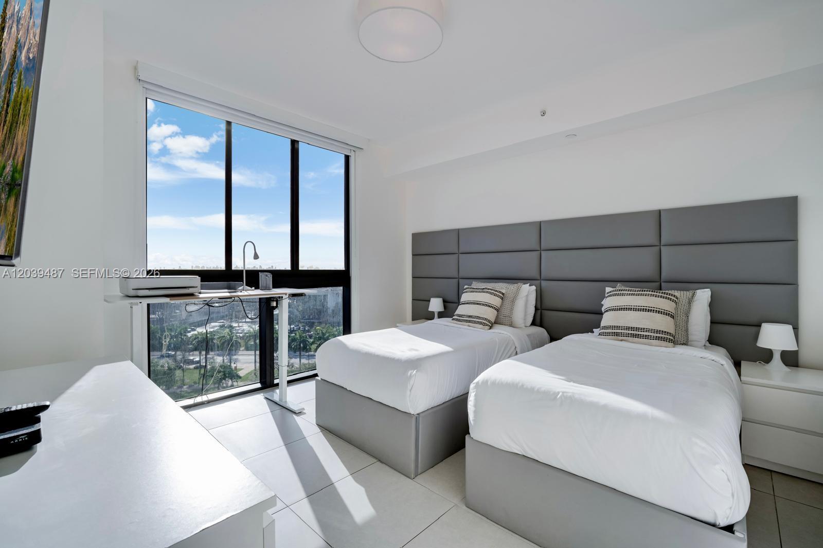 A bedroom features two twin beds, a gray paneled headboard, and floor-to-ceiling windows — 5350 NW 84th Ave # 909, Doral FL 33166, DORAL, FL