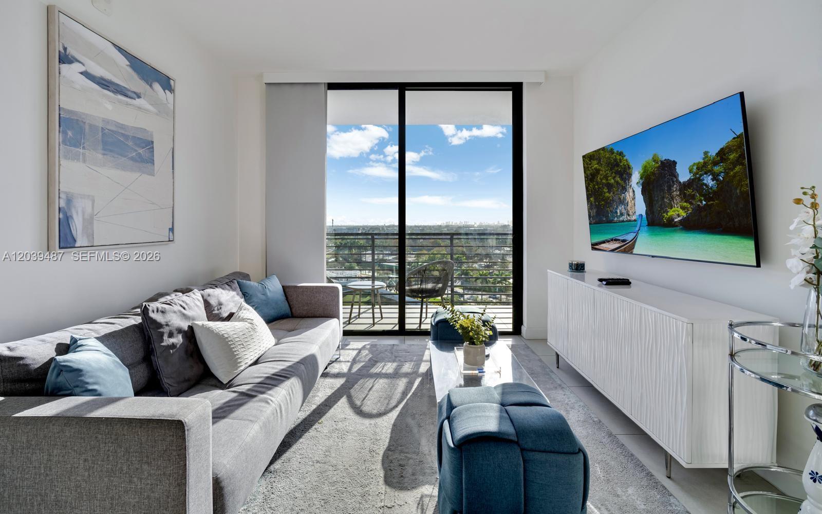 A modern living room features a gray sofa, a wall-mounted television, and a balcony view — 5350 NW 84th Ave # 909, Doral FL 33166, DORAL, FL