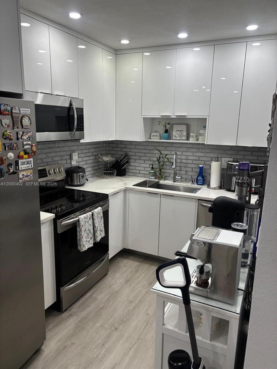 A modern kitchen features white glossy cabinets, stainless steel appliances, and a gray subway tile backsplash — 4050 NW 135th St # 1, Opa-Locka FL 33054, OPA-LOCKA, FL