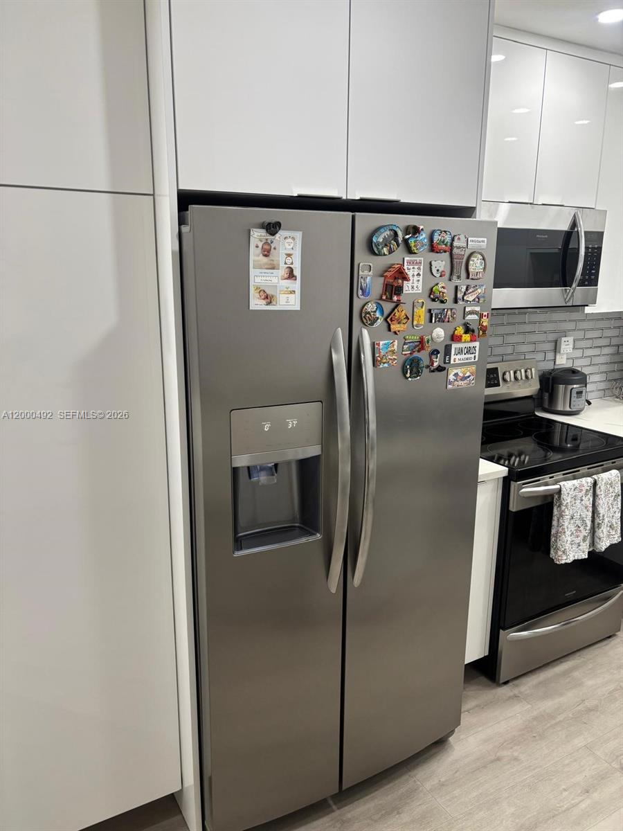 A stainless steel refrigerator stands in a modern kitchen with white cabinets and gray backsplash — 4050 NW 135th St # 1, Opa-Locka FL 33054, OPA-LOCKA, FL