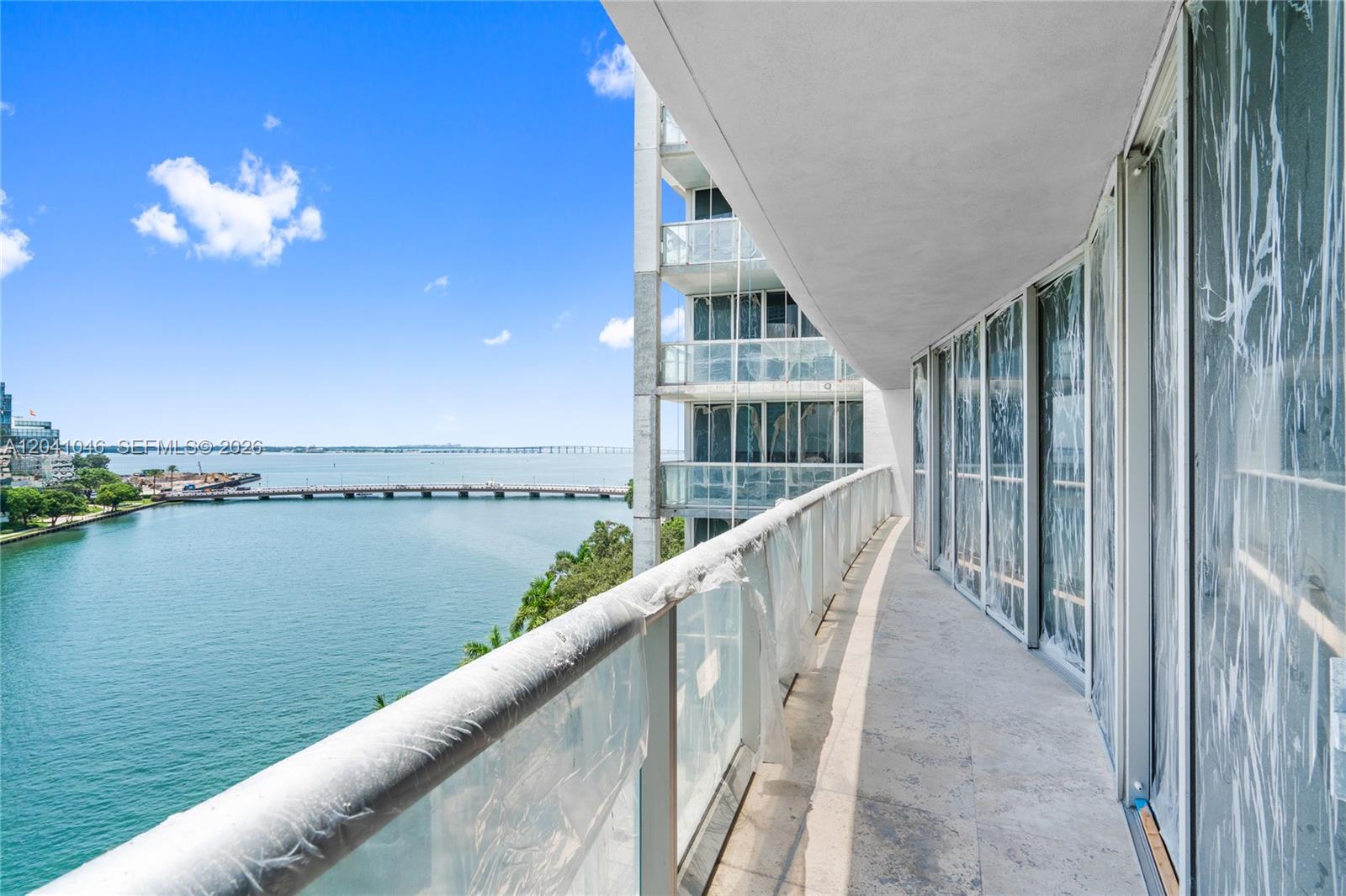 A balcony with glass railings overlooks a bay and a bridge under a blue sky — 495 Brickell Ave, Miami FL 33131, MIAMI, FL