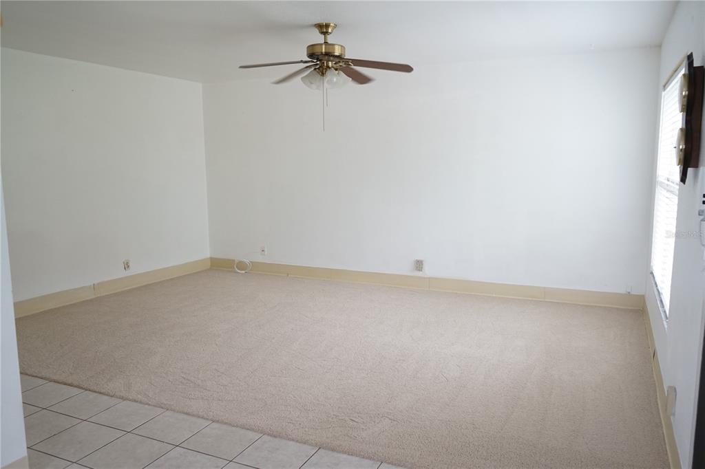 An empty living room features beige carpeting, white walls, a ceiling fan, and tile flooring — 101 CAMBRIDGE TRL UNIT 205, SUN CITY CENTER, FL