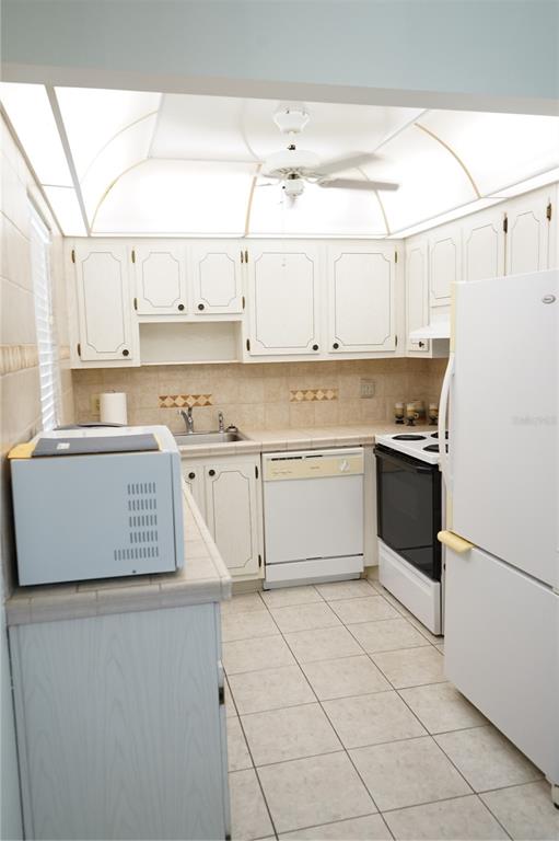 A kitchen features white cabinets, tile countertops, a ceiling fan, and white appliances — 101 CAMBRIDGE TRL UNIT 205, SUN CITY CENTER, FL