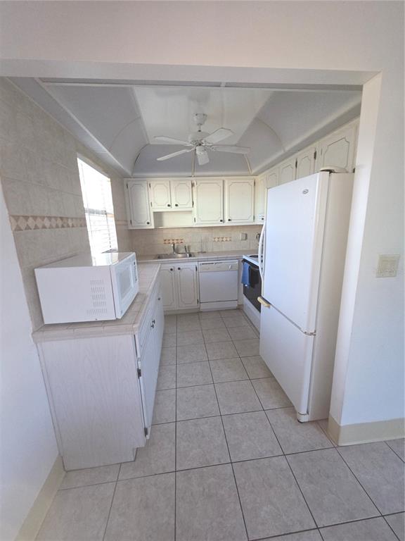 A galley-style kitchen features white cabinets, white appliances, tiled countertops, and light-colored floor tiles — 101 CAMBRIDGE TRL UNIT 205, SUN CITY CENTER, FL