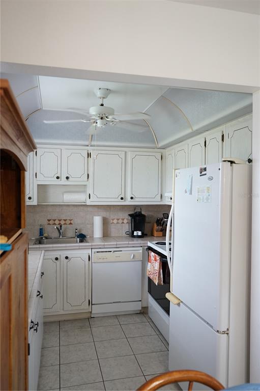A kitchen features white cabinetry, a tiled backsplash, a white dishwasher, and a ceiling fan — 101 CAMBRIDGE TRL UNIT 205, SUN CITY CENTER, FL