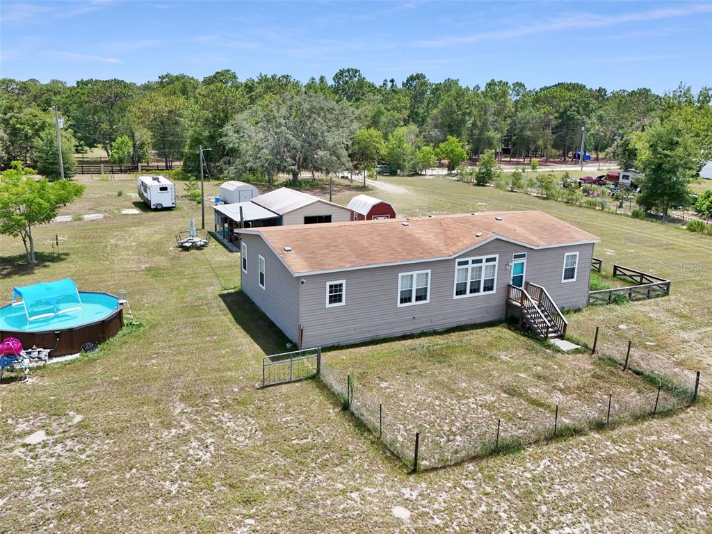 An aerial view shows a single-story house with a pool, sheds, and a fenced yard — 16947 AUBURNDALE LANE, SPRING HILL, FL