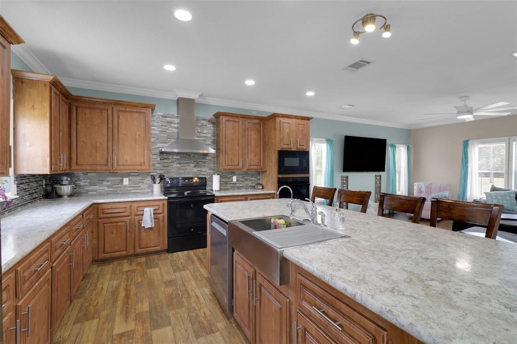 A kitchen with wood cabinets, stone backsplash, stainless steel appliances, and a large island — 16947 AUBURNDALE LANE, SPRING HILL, FL