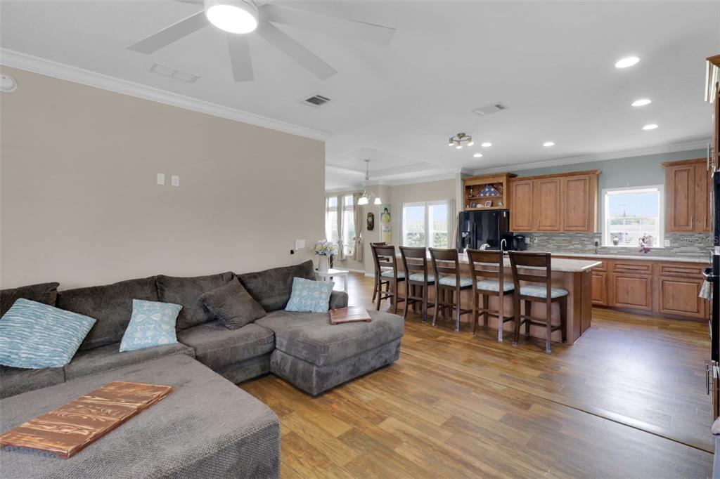 An open-concept living room with a sectional sofa flows into a kitchen with wooden cabinets — 16947 AUBURNDALE LANE, SPRING HILL, FL