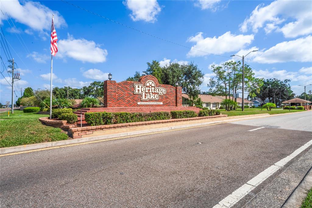 A brick monument sign for Heritage Lake stands beside a road under a blue sky — 4812 S SHEFFIELD DRIVE UNIT 5, NEW PORT RICHEY, FL