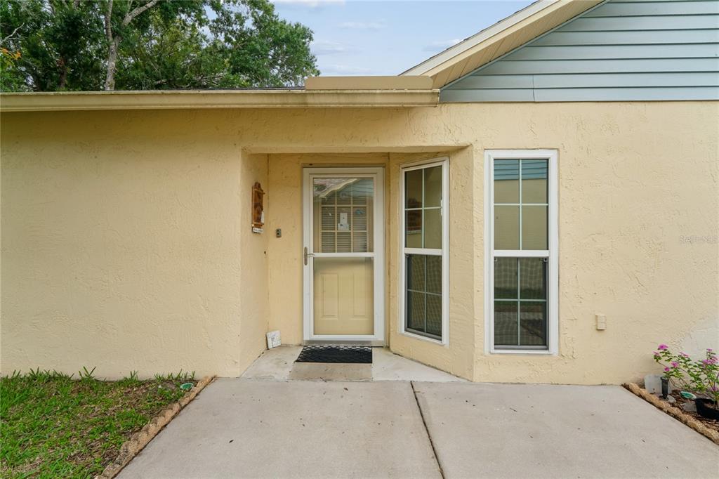 A beige stucco house exterior features a front door, a bay window, and concrete walkway — 4812 S SHEFFIELD DRIVE UNIT 5, NEW PORT RICHEY, FL