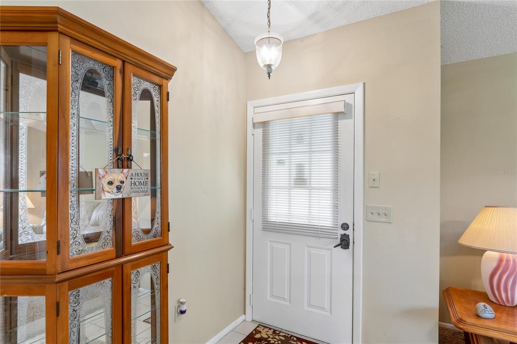 An entryway features a wooden display cabinet, a white door with blinds, and a pendant light — 4812 S SHEFFIELD DRIVE UNIT 5, NEW PORT RICHEY, FL