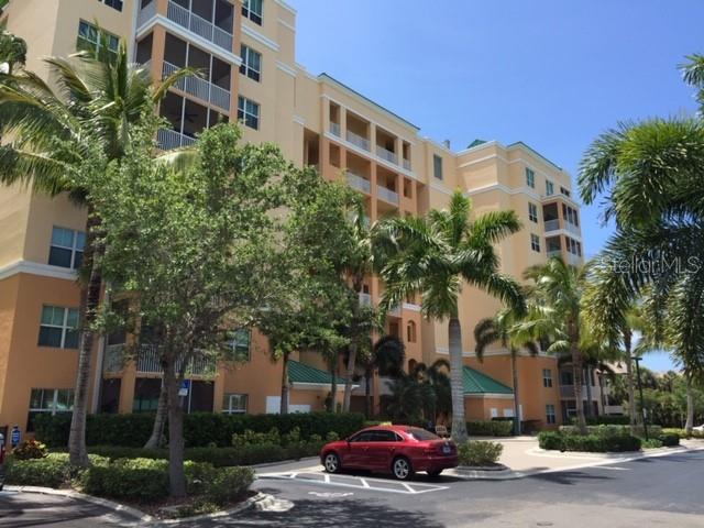 A red sedan is parked in front of a multi-story tan apartment building with palm trees — 2060 MATECUMBE KEY ROAD UNIT 2104, PUNTA GORDA, FL