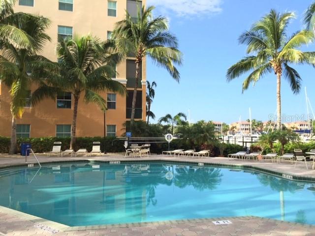 A swimming pool sits in front of a multi-story building with palm trees and a marina — 2060 MATECUMBE KEY ROAD UNIT 2104, PUNTA GORDA, FL