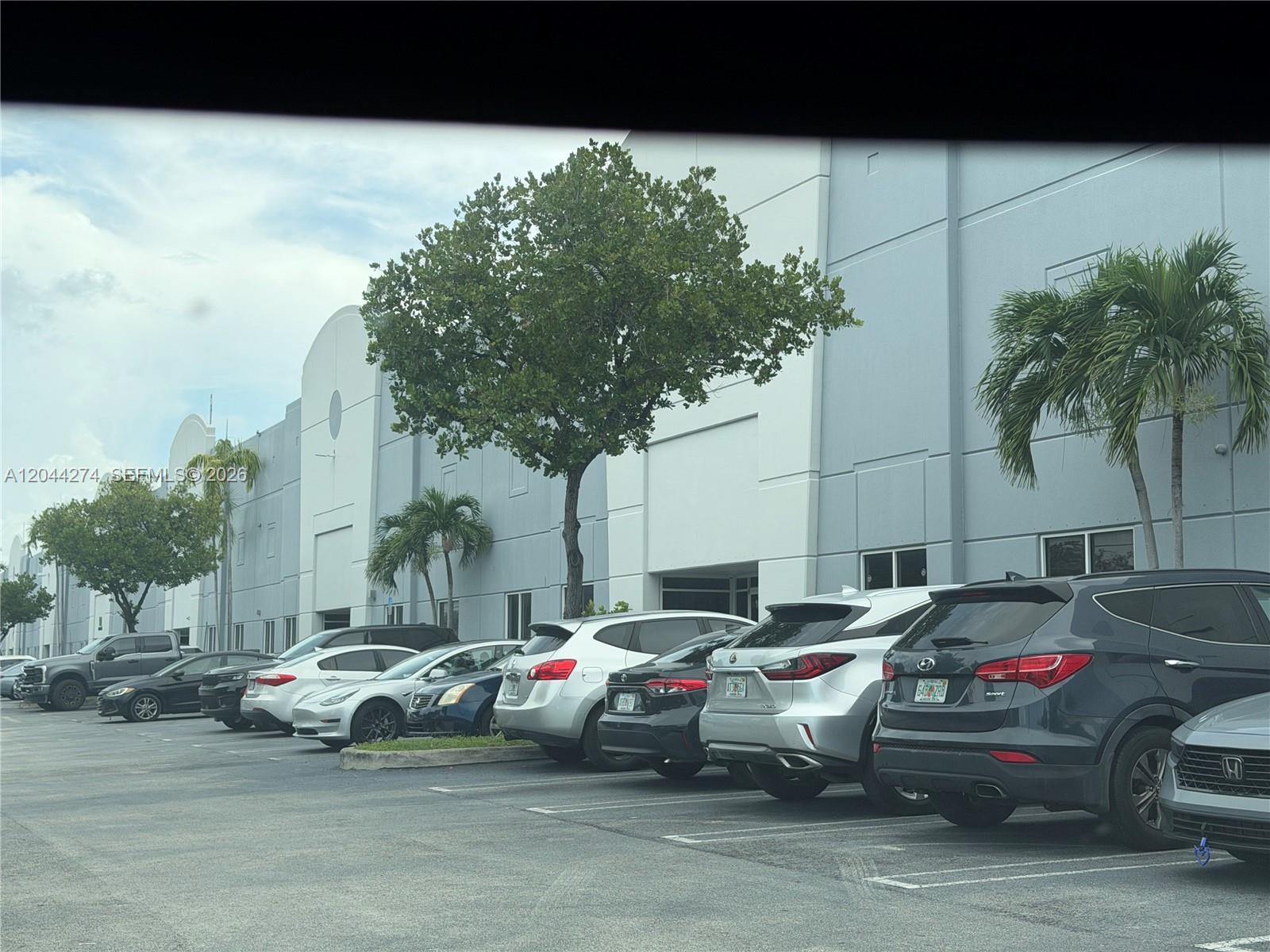 A row of parked cars sits in front of a large, light-colored industrial warehouse building — 10871 NW 122nd St # 30, Medley FL 33178, MEDLEY, FL