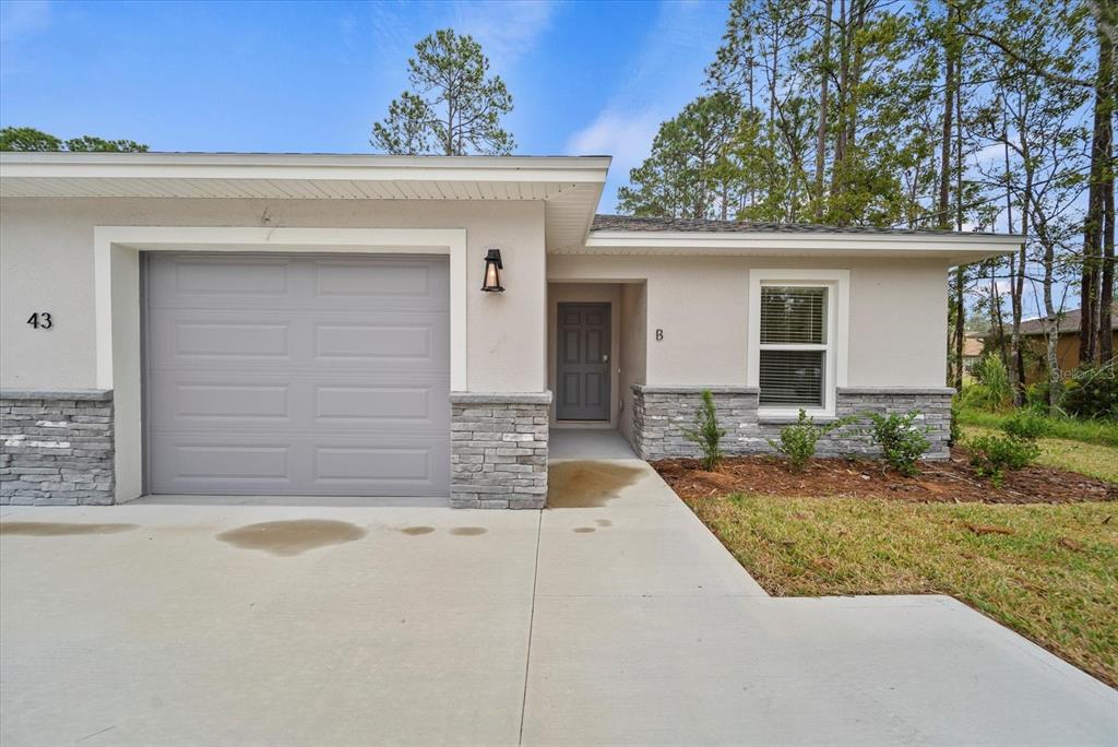 A single-story house exterior features a gray garage door, stone veneer, and a front entrance — 43 PONCE DELEON DRIVE UNIT B, PALM COAST, FL