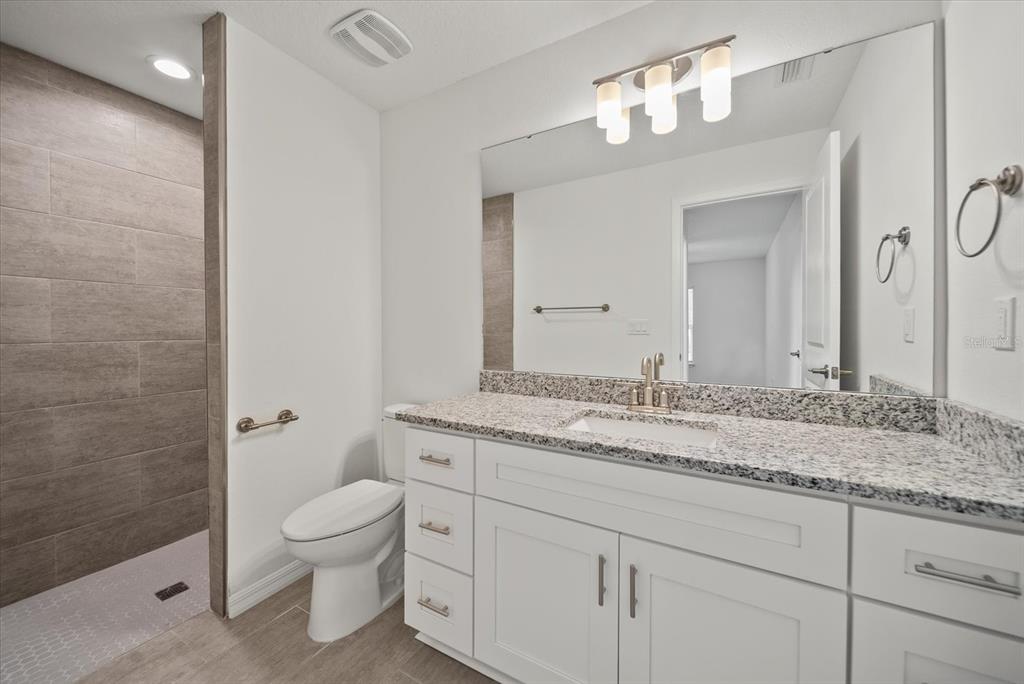 A bathroom features a white vanity with granite countertops, a toilet, and a tiled walk-in shower — 43 PONCE DELEON DRIVE UNIT B, PALM COAST, FL