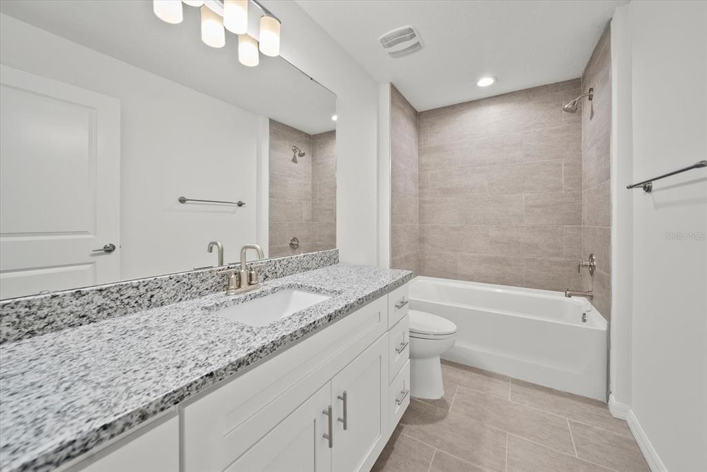 A bathroom features a white vanity with granite countertop, a tub-shower combo, and tiled flooring — 43 PONCE DELEON DRIVE UNIT B, PALM COAST, FL