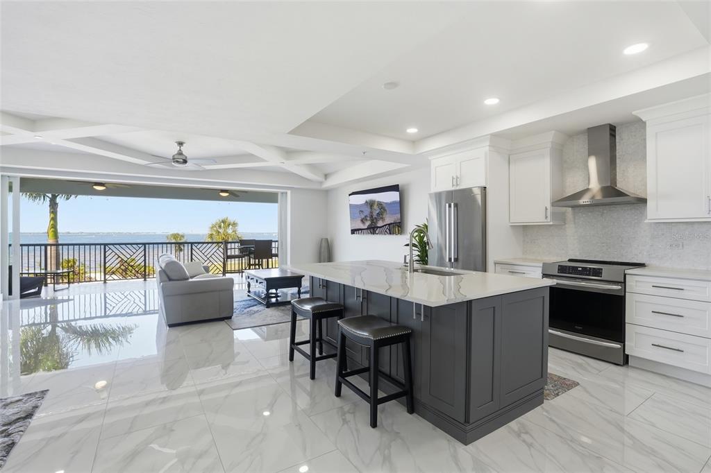 A modern kitchen with a dark gray island overlooks a living area and waterfront balcony — 1425 PARK BEACH CIRCLE UNIT 124, PUNTA GORDA, FL